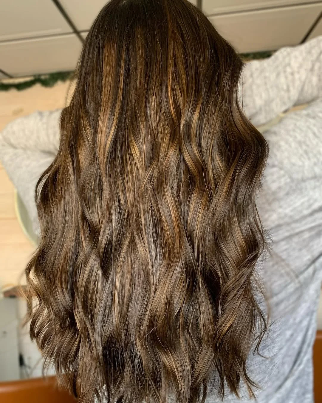summer money piece hair color for women 2026 Rich Brown Waves with Subtle Peekaboo Highlights