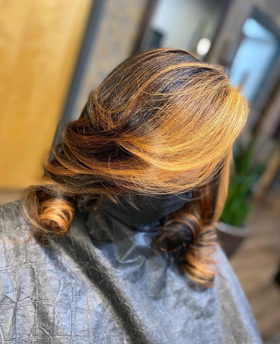 Warm caramel blonde hair swept sideways into low curls with darker brown strands