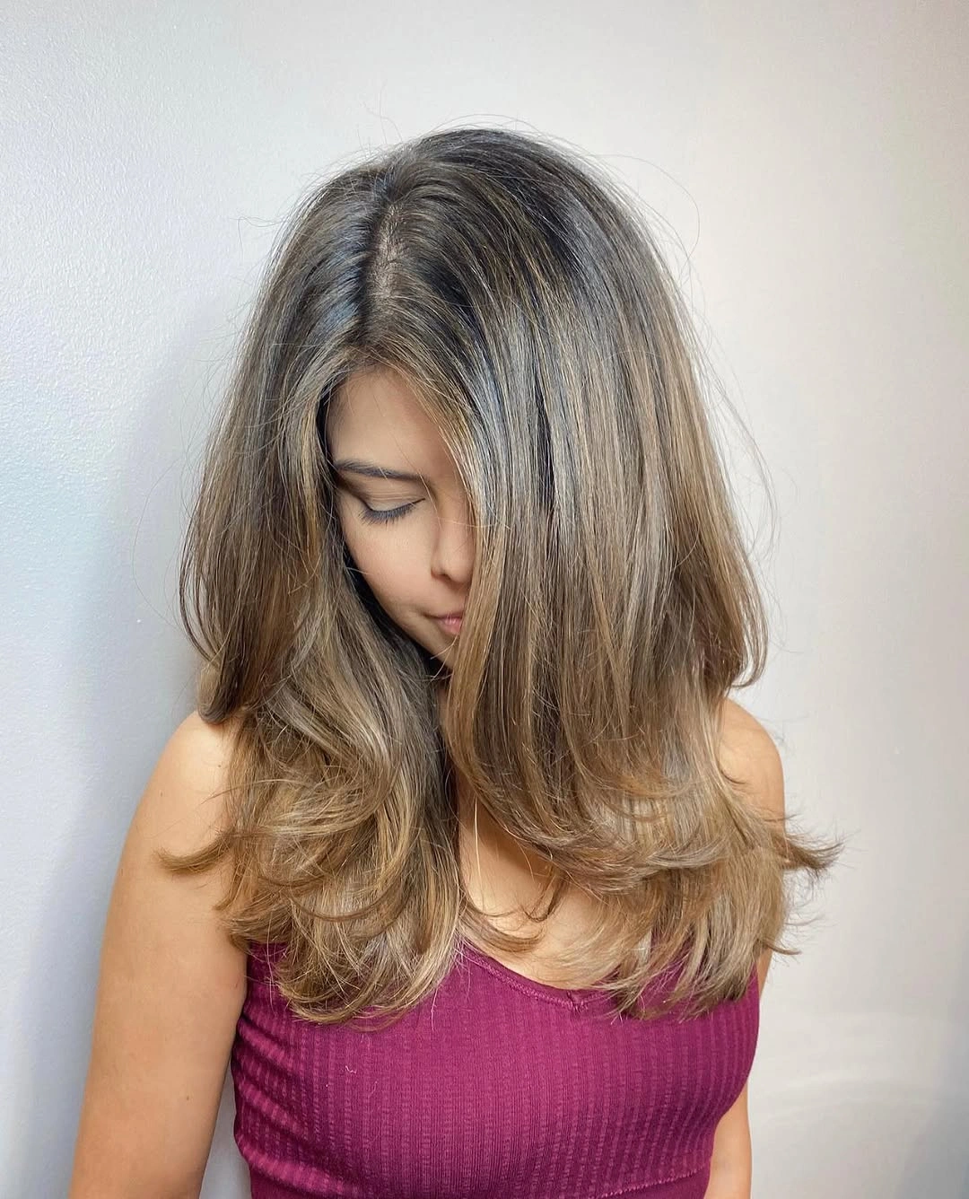 Voluminous beige ash blonde layered hair with darker roots and feathered ends