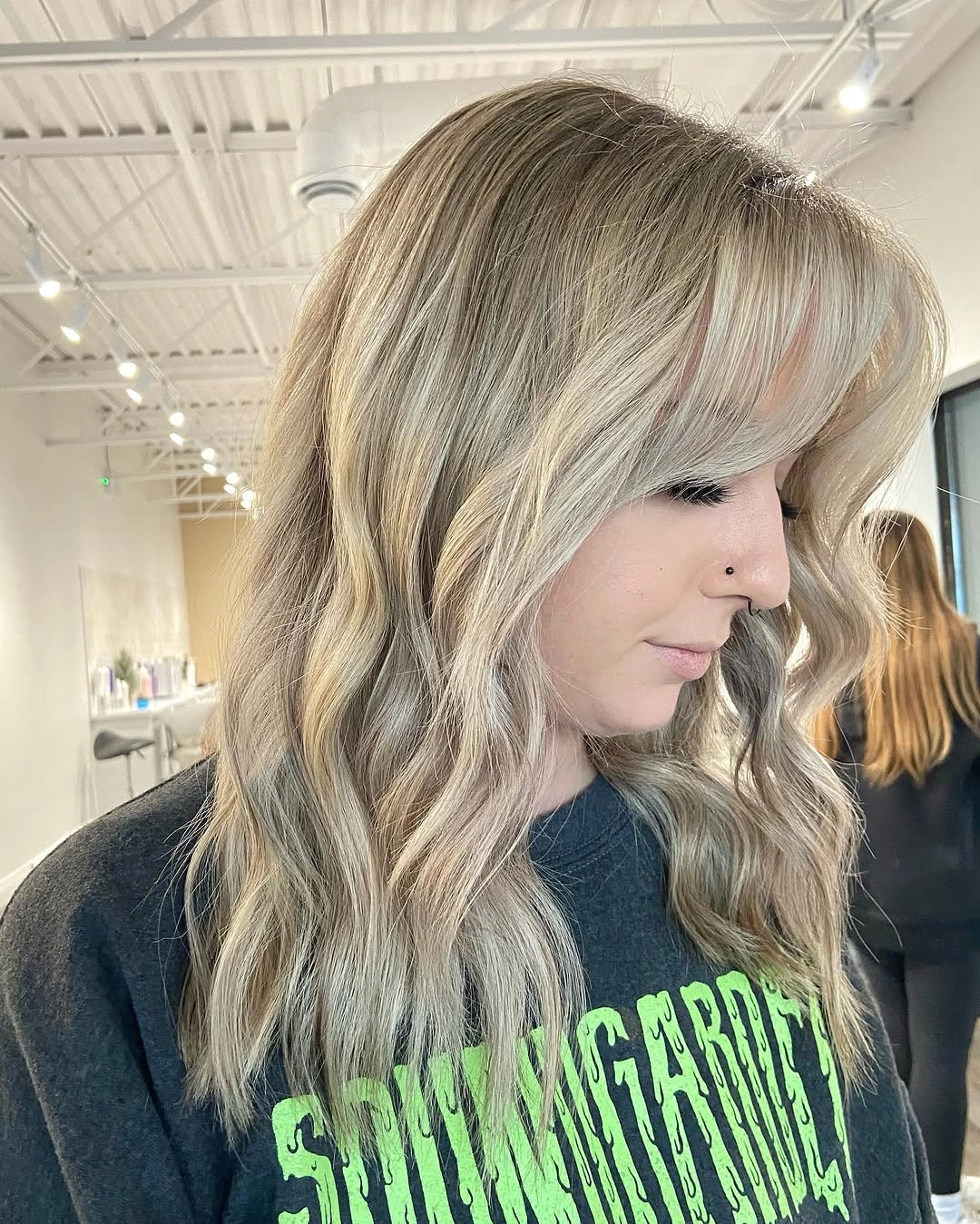 Medium length creamy blonde waves with beige tones and side swept bangs