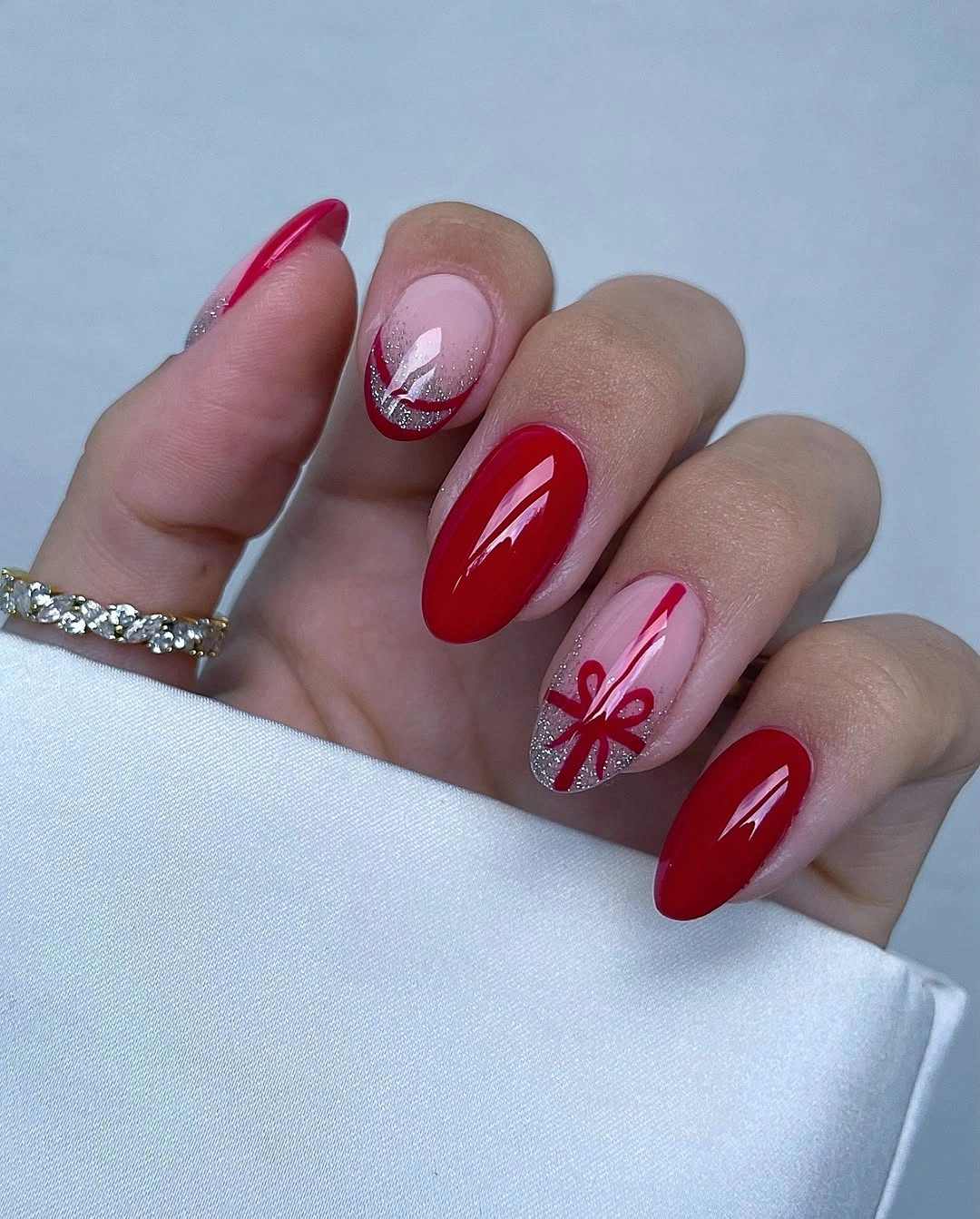 Glossy red almond nails with silver glitter tips and painted ribbon bow