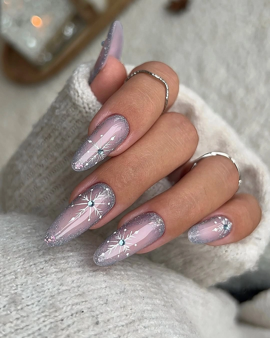 Long pink almond nails with silver glitter edges and white snowflake designs
