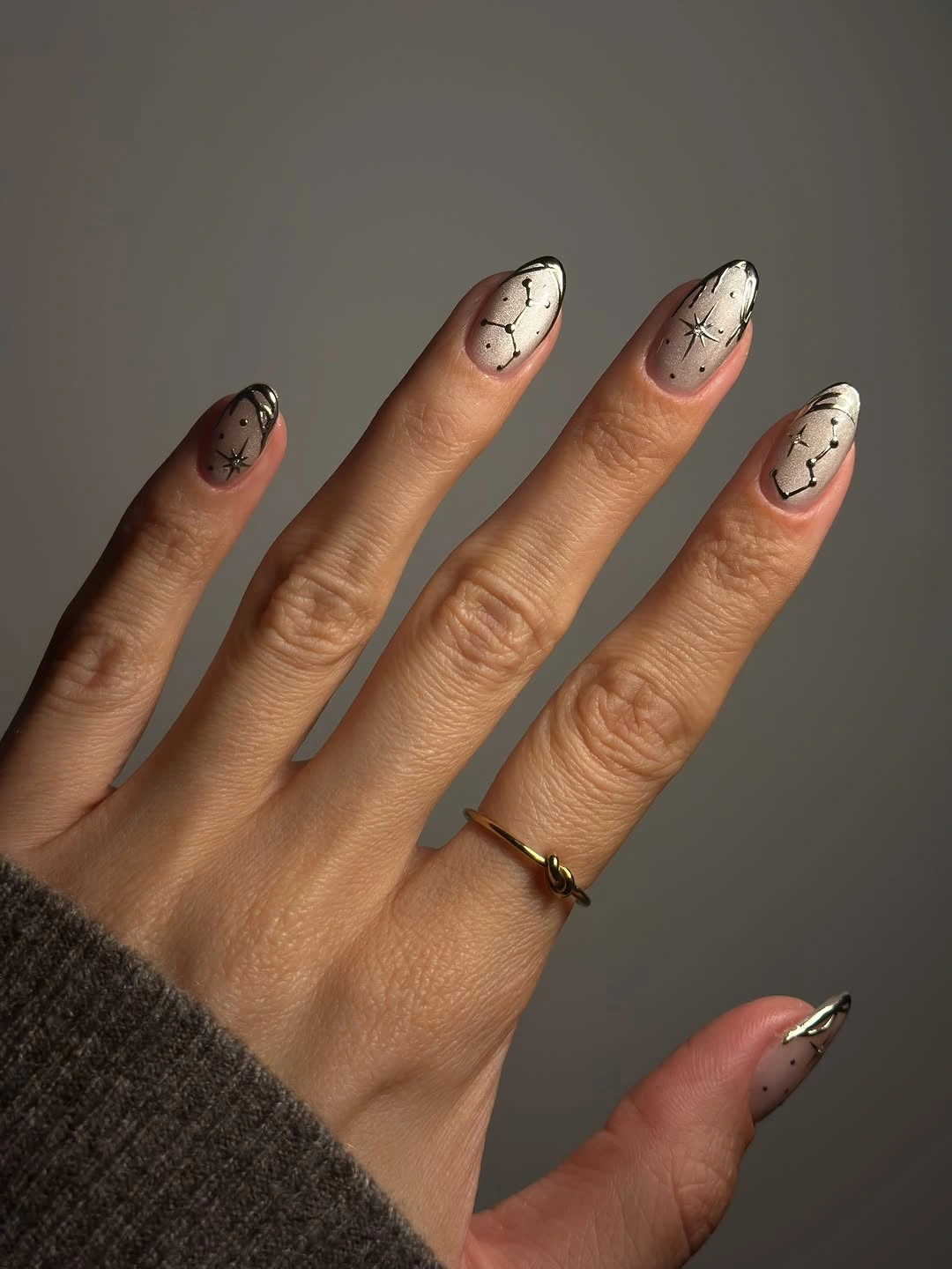Neutral almond nails with fine black starburst lines and dark metallic edges