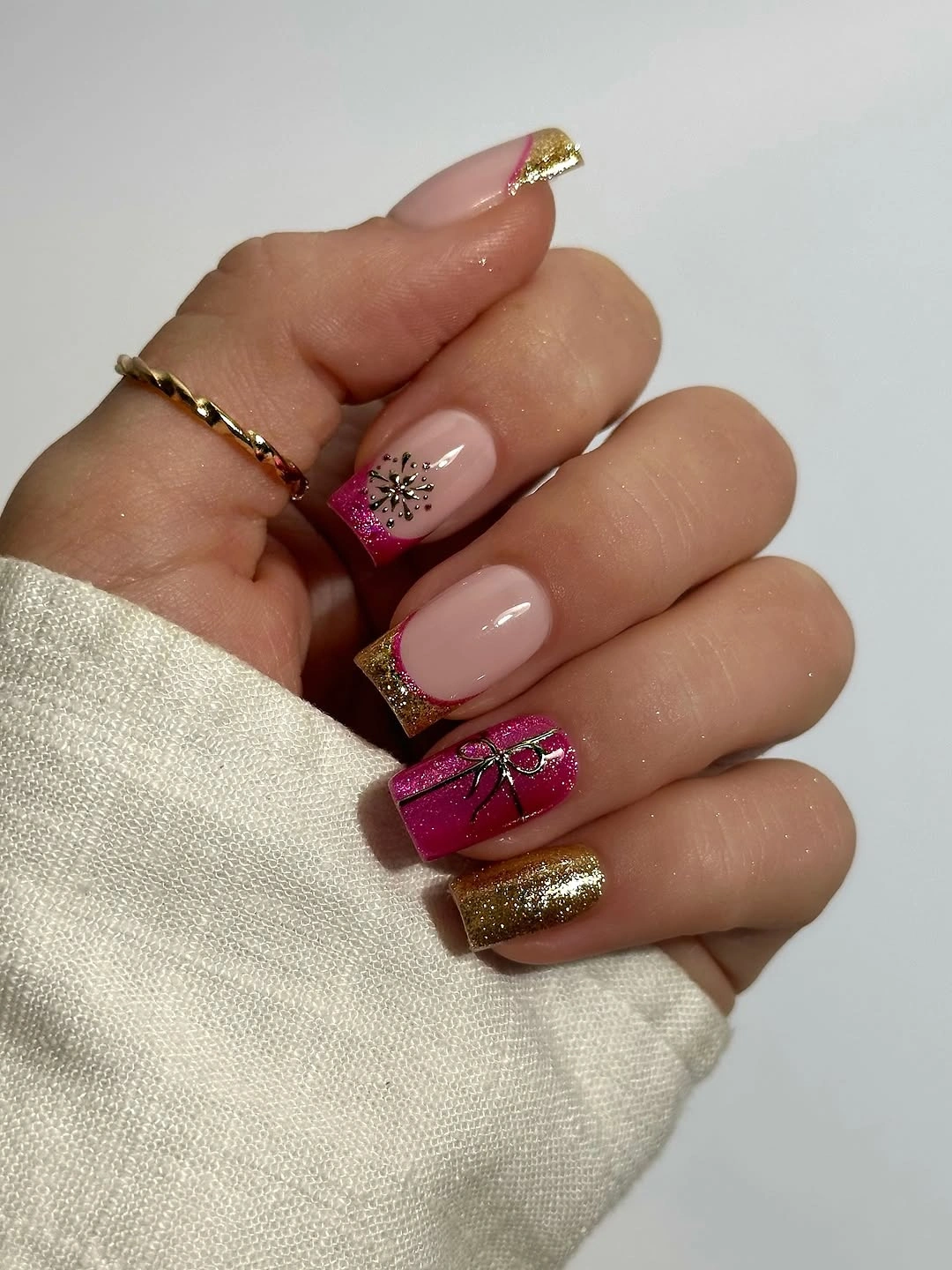 Pink and gold nails with glittering accents and tiny dark bow