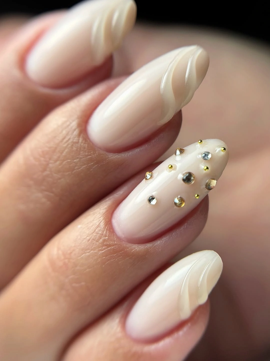 Creamy ivory almond nails with raised flowing ridges and reflective studs