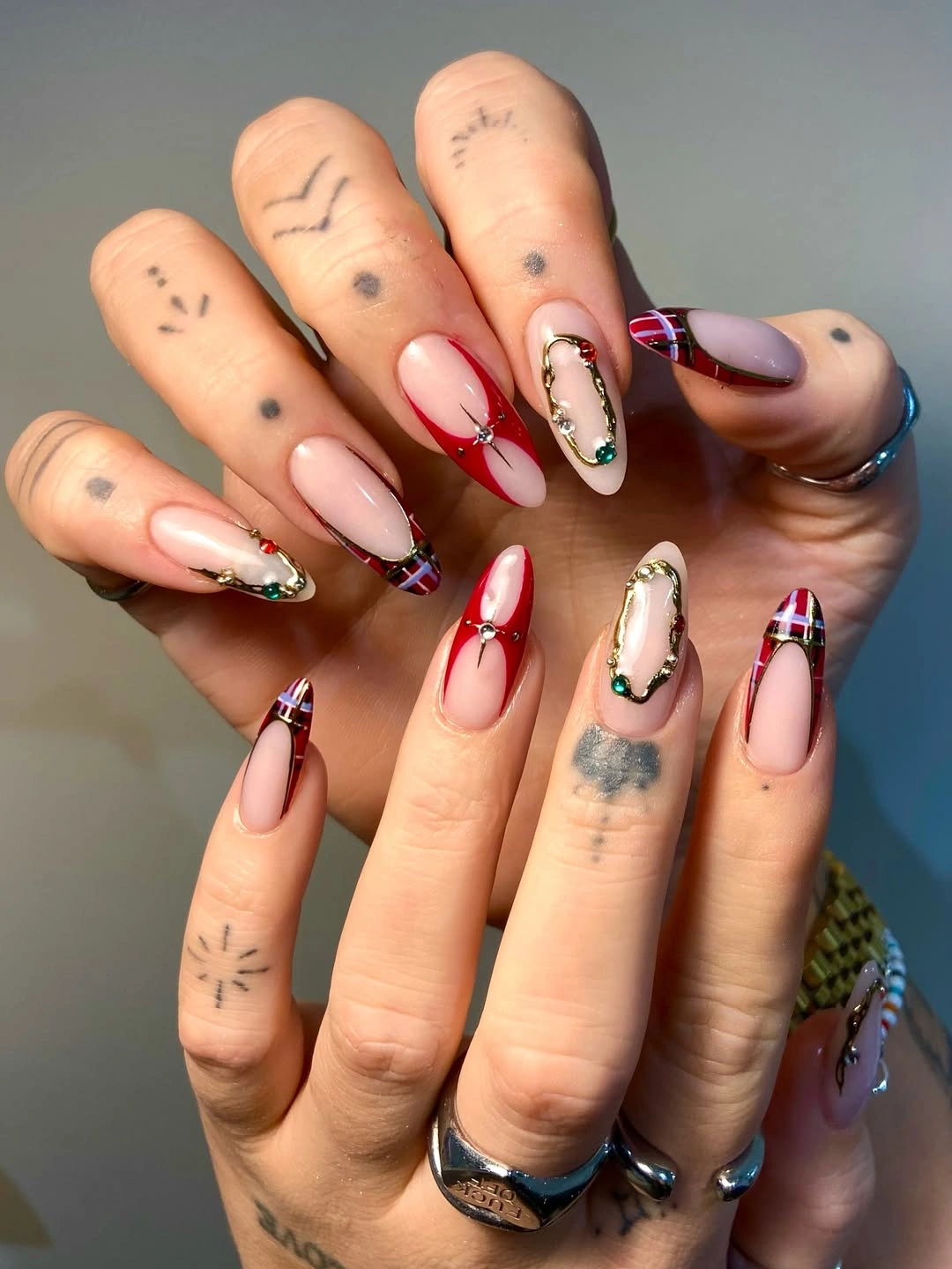 Nude pointed nails with red accents plaid tips and gold decorations