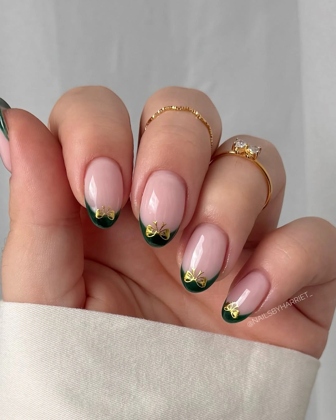 Blush pink almond nails with dark green tips and gold bows