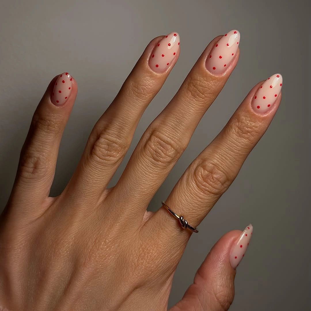 Short almond nails with sheer blush pink bases and scattered red dots