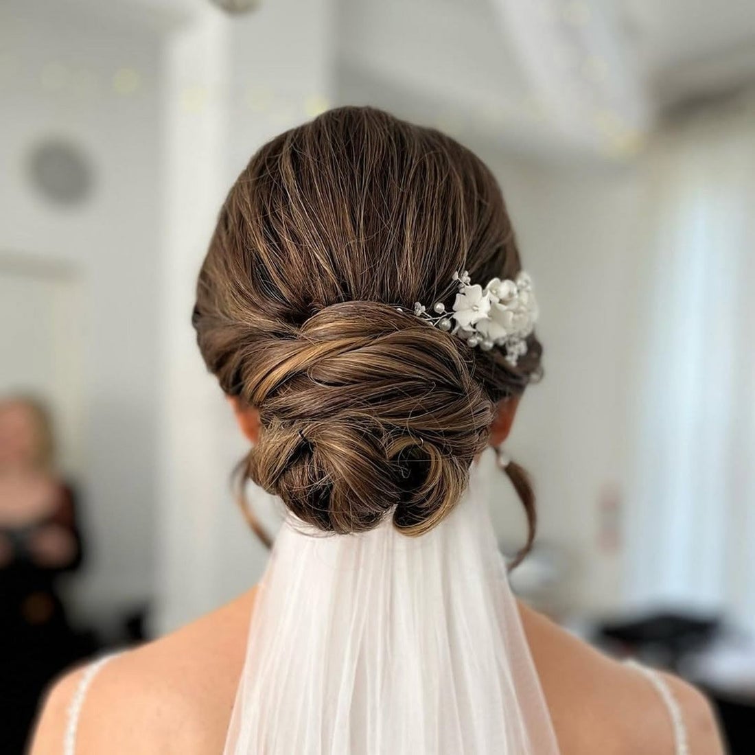 Low Dark Brown Twisted Bun With Floral Accessory — Trendy Wedding Bun